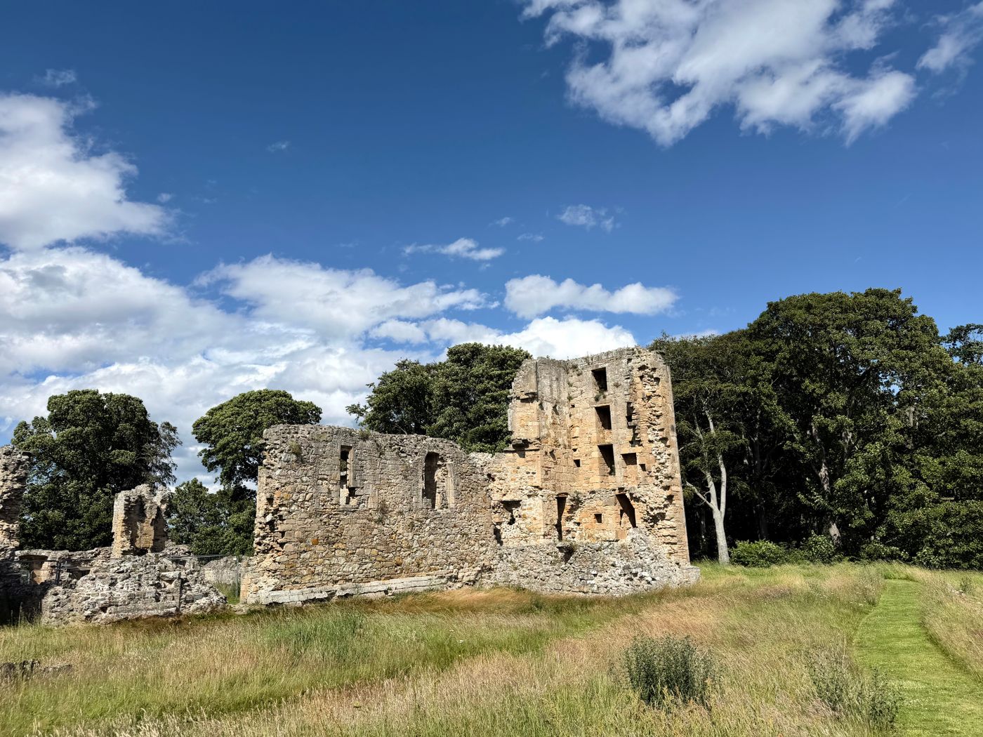 Historic ruins of Duffus Castle surrounded by lush greenery under a bright blue sky.